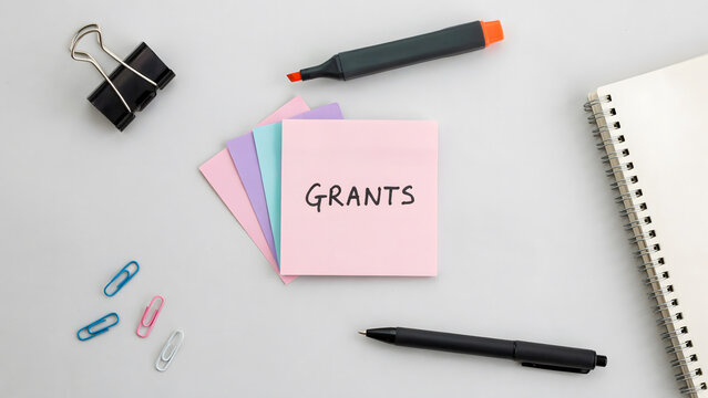 Sticky note with the word grants written on a white office desk surface