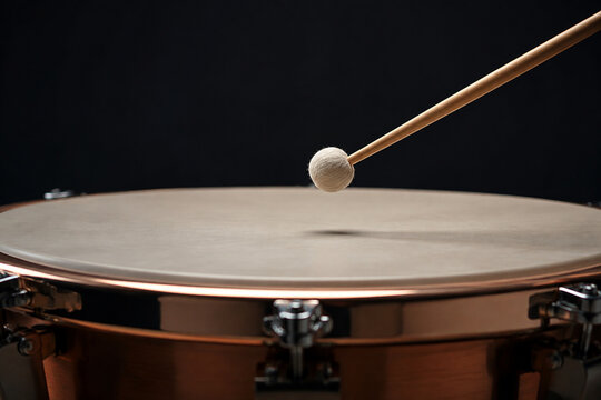 Drumstick poised just above the skin of a timpani drum.