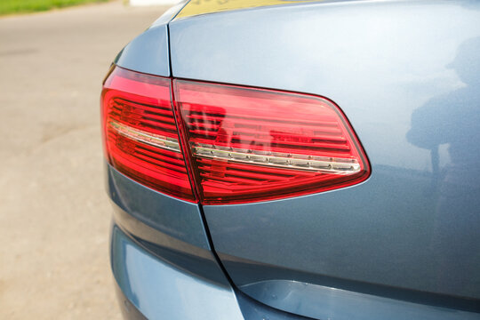 Close-up of a car's rear light assembly with red and clear lenses, highlighting the design on a blue vehicle parked on a paved surface