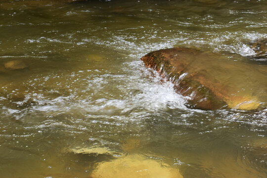 clear flowing stream of shadow water rushing over smooth rocks in a natural outdoor