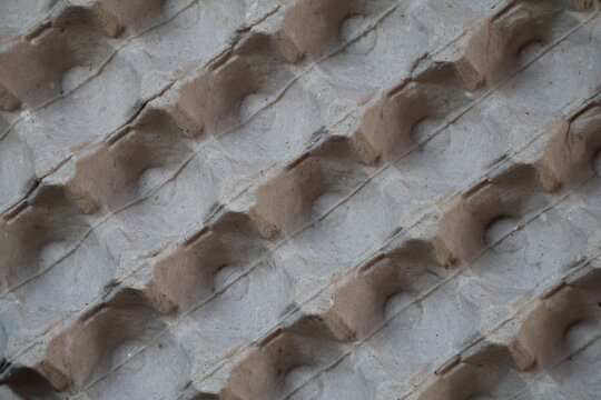 Closeup of pressed recycled cardboard egg tray texture, highlighting rough fibers, natural paper pulp, sustainable packaging, and earthy material details.