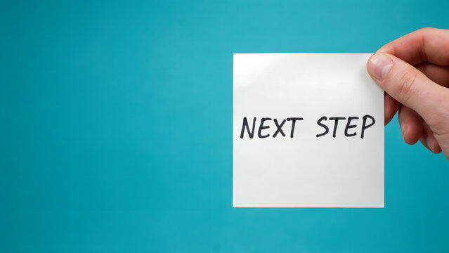A hand holding a white paper note with the text next step on a blue background