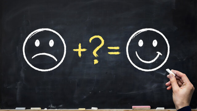 A hand drawing a happy face to transform a sad face on a black chalkboard