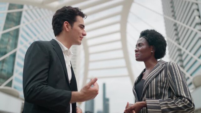 Two professionals converse warmly near modern architecture. Their smiles suggest mutual respect and active engagement
