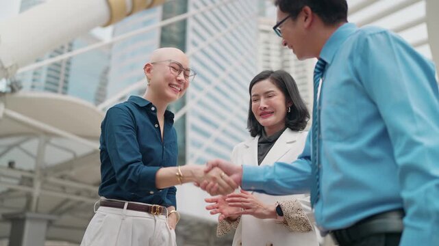 Business people shake hands outdoors near skyscrapers. They smile warmly, suggesting a successful agreement or greeting