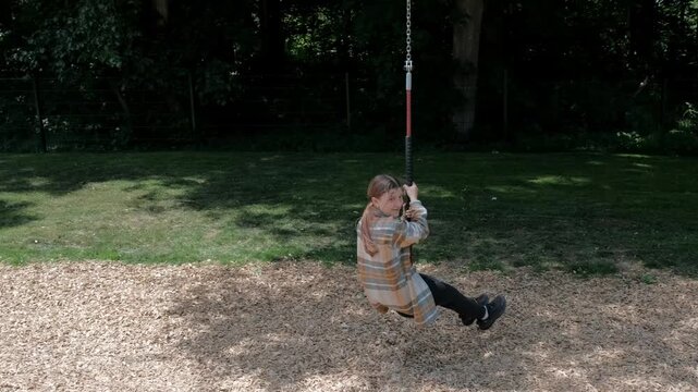 Side view of a happy child holding onto a zip line rope and sliding through the air at an outdoor playground.
