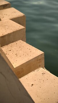 Minimalist close-up of geometric concrete promenade blocks next to deep blue sea water. Concept of coastal architecture, urban design, and solid barriers. 4K vertical video