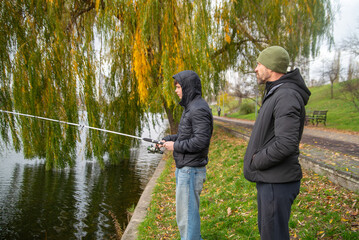 Naklejka premium Father and Son Fishing Together by a Lake in Autumn Park