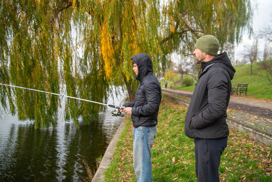 Father and Son Fishing Together by a Lake in Autumn Park
