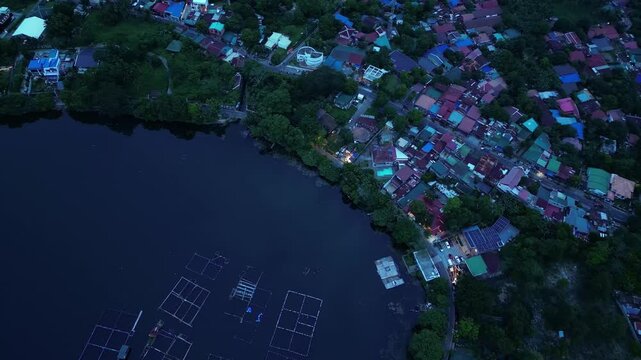 Forward aerial frame capturing Sampaloc Lake and fishponds surrounded by the urban landscape of San Pablo City, Laguna, Philippines, with rural roads under blue hour.
