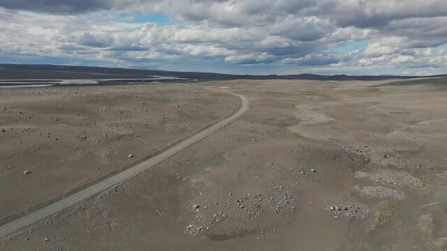 A cinematic aerial shot following a remote dirt road through the barren, rocky landscape of Iceland. Captures the isolation and raw beauty of the volcanic highlands.