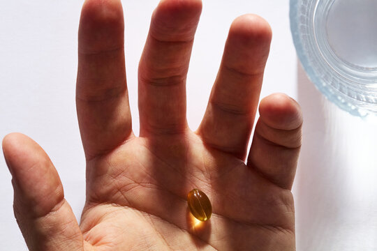 Close-Up of Hand Holding Yellow Vitamin Capsule Beside Glass of Water