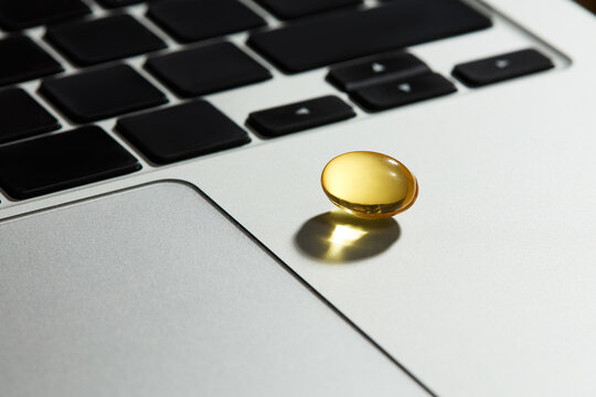 Yellow Fish Oil Supplement Capsule on Laptop Computer