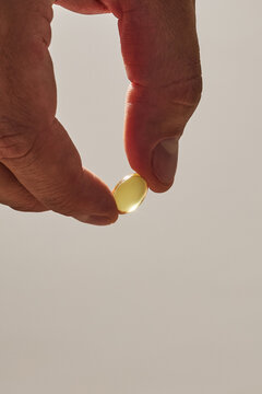 Close-up of a hand holding a golden vitamin gel capsule supplement