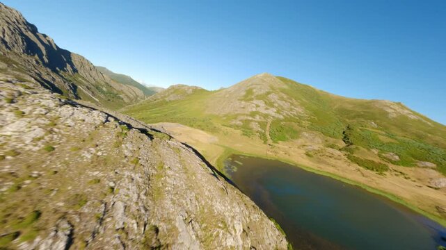 Dynamic FPV drone flight capturing the rugged beauty of the Leon mountains and a pristine alpine lake under a clear blue sky. Ideal for travel and sustainability content.