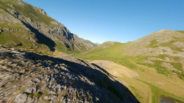 Dynamic aerial FPV drone perspective flying over rugged mountain peaks and a clear alpine lake in Leon, Spain. Ideal for travel, adventure, and sustainability content.