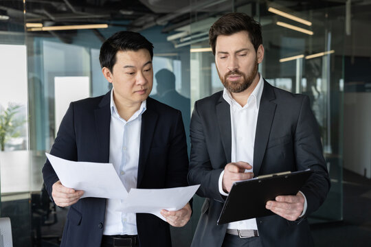 Diverse business professionals reviewing important documents and planning strategy, standing in a modern corporate office interior, fostering teamwork and professional cooperation