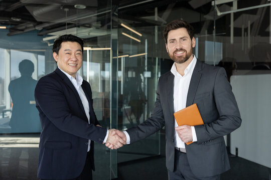 Diverse businessmen smiling and shaking hands in a modern office, celebrating a successful partnership and closed deal that reflects trust, collaboration and professional achievement