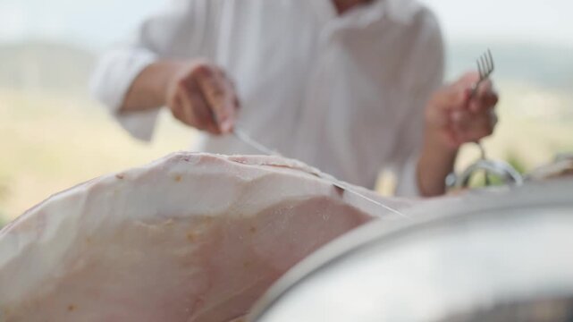 Professional chef carving a leg of cured ham outdoors