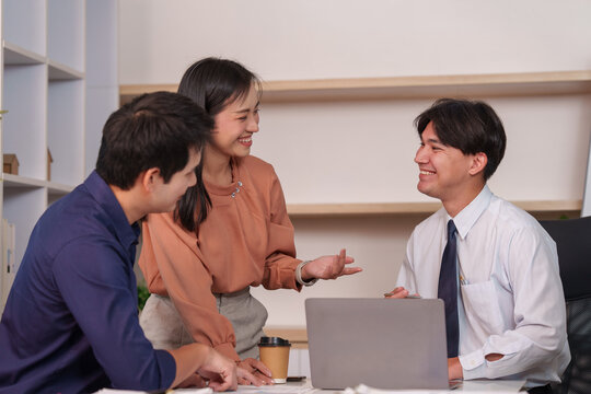 Asian business team smiling while discussing artificial intelligence software on laptop in office