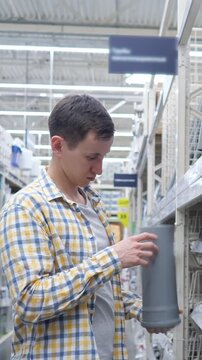 Careful male customer in a plaid shirt browsing the plumbing section of a large home improvement store, selecting pvc pipes and fittings for a renovation project or plumbing repair