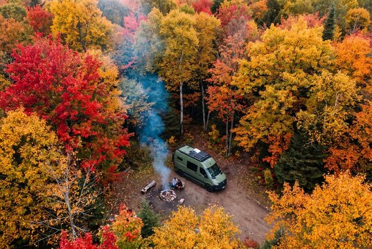 Camper van and campfire in colorful autumn forest