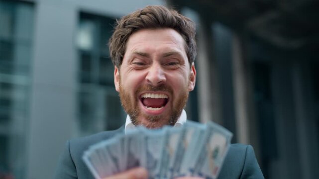 Happy middle-aged Caucasian business man holding money cash yelling celebrating financial success rejoicing winning finance reward prize income casino win businessman male hold dollars yell in city
