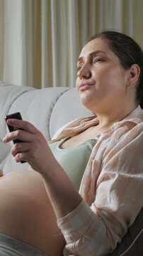 Emotional pregnant woman sitting on the couch and crying while watching a sad drama or romantic movie on television, showing her sensitivity and hormonal changes during pregnancy