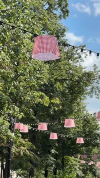 Outdoor red and white checkered lampshades hanging among trees under a blue sky