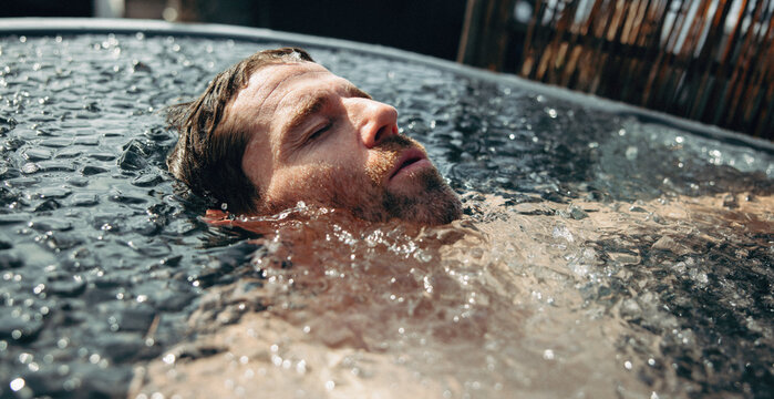 A water-focused man enjoys an outdoor ice bath for recovery and wellness.