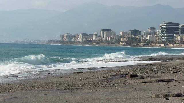 Coastal cityscape and sea waves with a mountainous backdrop under a clear sky