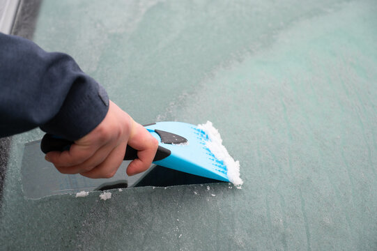 Driver is removing snow from car windshield with ice scraper and broom, clean car window from icy frost, winter season
