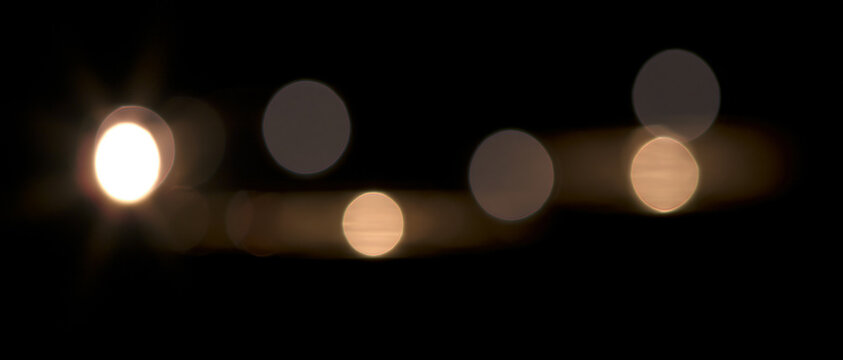 Festive warm glowing fairy lights and abstract bokeh garland on black background. Defocused night lights with optical lens flare for Christmas overlay and festive backgrounds.