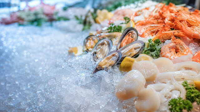 Assorted fresh seafood including shrimp, mussels, scallops and squid arranged on crushed ice with lemon wedges and parsley garnish at a market counter.