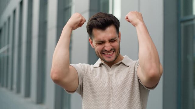Happy young Caucasian business man yelling celebrate rejoicing winning raising hands in city near office building. Businessman male champion lucky worker guy looking at camera win yell rejoice success