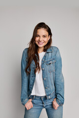 A cheerful teenage girl poses confidently in a denim jacket, white shirt, and jeans