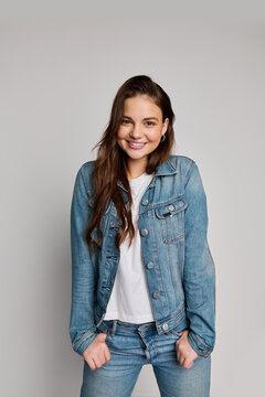 A cheerful teenage girl poses confidently in a denim jacket, white shirt, and jeans