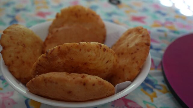 Golden arepa de huevo arranged in a white bowl, captured in a close-up shot on a bright, patterned tablecloth. Soft daylight highlights the crispy texture, perfect for food concepts.