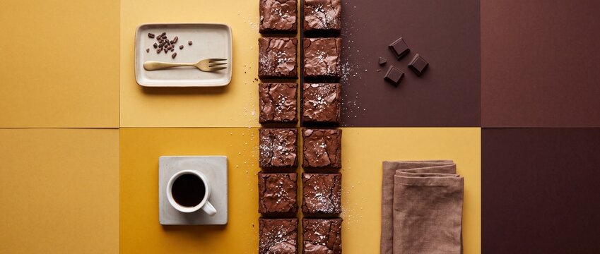 Rich dark chocolate brownies with sea salt sprinkled on top, served with coffee and chocolate squares on a warm yellow and brown background.