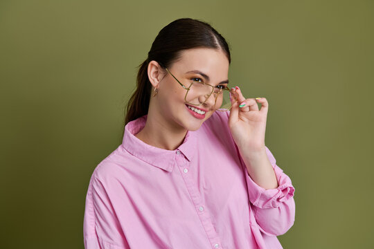 Stylish teenager in pink shirt poses playfully with glasses against green backdrop