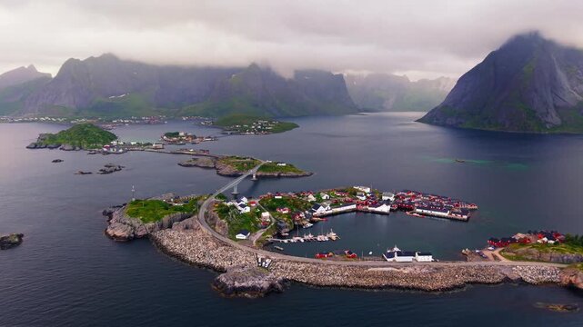 Drone panorama over Hamn&oslash;y, revealing its sheltered harbor, coastal islands and towering mountains rising above the Lofoten Islands in Norway