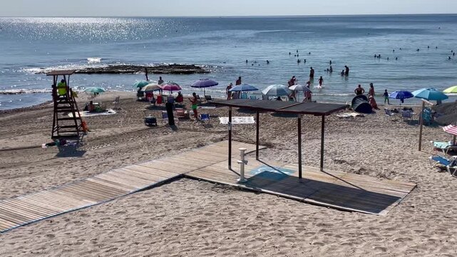 Playa, sol, ba&ntilde;istas, sombrilla en arena, socorrista y vacaciones de verano en el mar y horizonte costa y acceso entrada de madera tablas