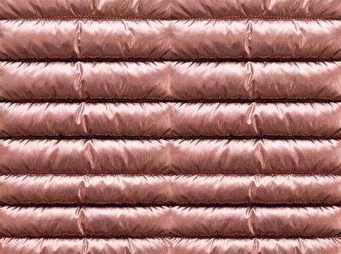 Shiny rose gold quilted puffer fabric texture with horizontal padded channels, perfect for fashion and jacket backgrounds.