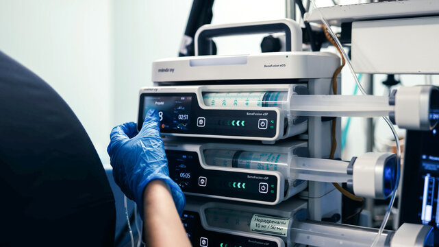 Medical professional in a sterile glove adjusts infusion and syringe pumps in a modern hospital operating room during patient treatment.
