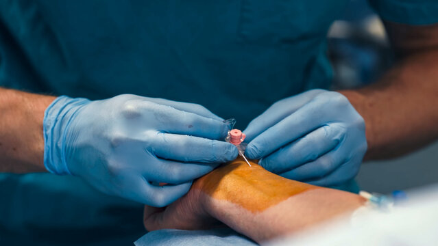 Close-up of a peripheral venous catheter being inserted into a patient's hand by a medical professional.