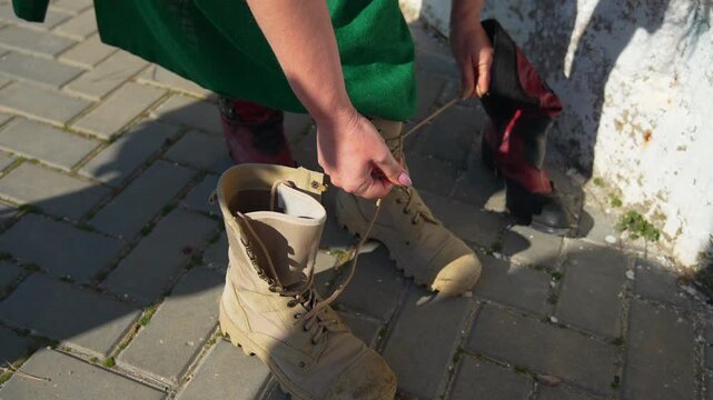 Boots lacing combat woman wearing a green dress tying laces on beige tactical boots on a paved outdoor walkway in the sun
