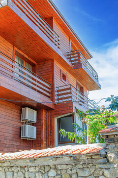 A modern wooden multi-story building features balconies and air conditioning units under a clear blue sky.