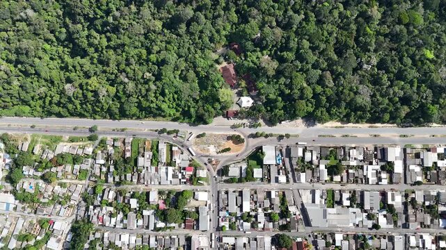 Aerial footage of a winding road and intersection bordering a lush tropical rainforest and a dense urban community in Brazil.