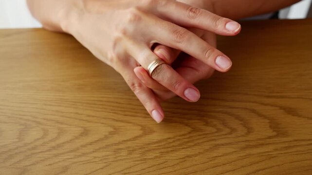 Close-up of a woman removing a wedding ring from her finger and leaving it on a wooden table, symbolizing divorce, separation, broken marriage, relationship breakdown and the end of marital commitment