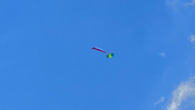 A parachutist is flying under a canopy with a huge, fluttering flag against the backdrop of a blue sky. A spectacular aerial stunt and an extreme sport.

